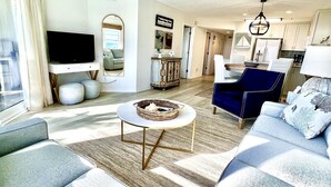 A modern living room with a sofa, a coffee table, a TV, and a dining area with a table and chairs. - Luxury Gulf-Front 2BR 2BA Pet-Friendly Maravilla Resort Condo - Stunning Views (Miramar Beach)