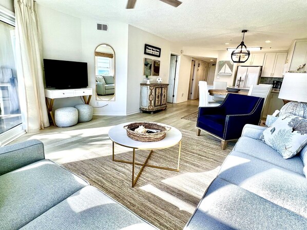 A modern living room with a flat-screen TV, a round coffee table, and a sofa. There is a dining area with a table and chairs. - Luxury Gulf-Front 2BR 2BA Pet-Friendly Maravilla Resort Condo - Stunning Views (Miramar Beach)