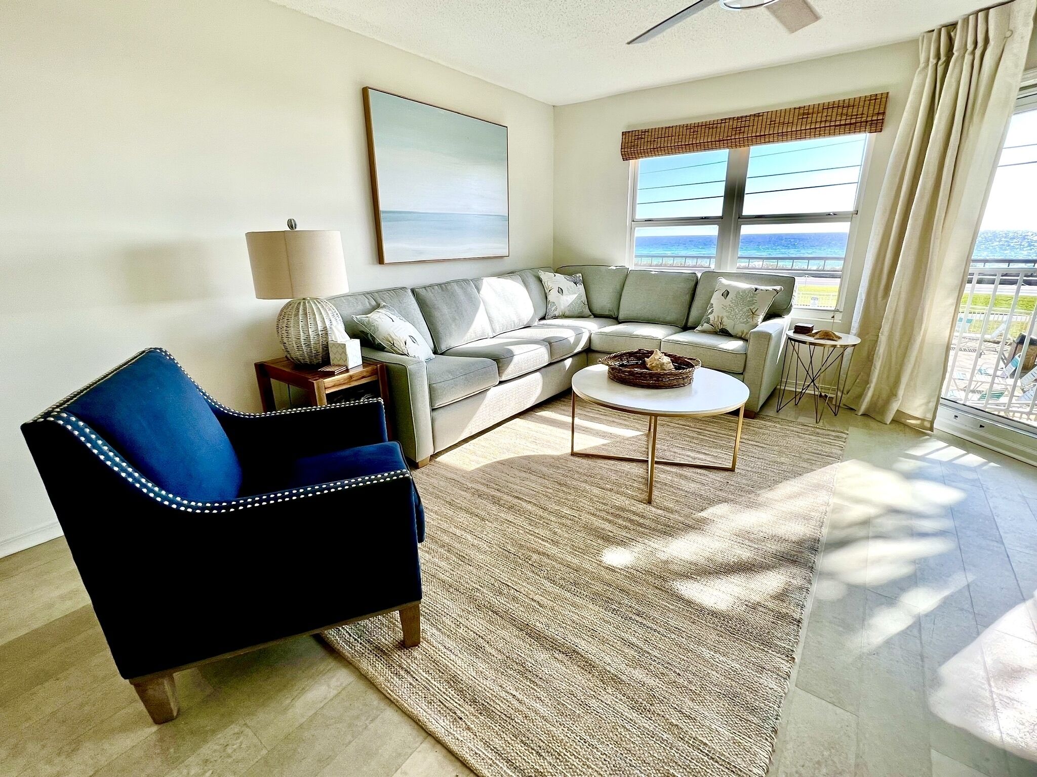A living room with a sofa, armchair, coffee table, and a view of the ocean.