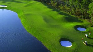 A golf course with water hazards, sand bunkers, and a forested area in the background. - Luxury Gulf-Front 2BR 2BA Pet-Friendly Maravilla Resort Condo - Stunning Views (Miramar Beach)