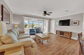 A spacious living room with a wooden floor, a sofa, a coffee table, a TV, and a ceiling fan. - Private Pool, Bay Views & Pet-Friendly | The Salty Snapper (Saint George Island)