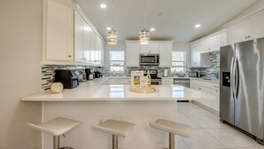 A modern kitchen with white cabinetry, stainless steel appliances, and a central island with bar stools.