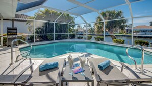 A pool area with lounge chairs, a grill, and a covered seating area.