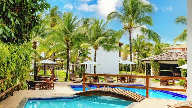 A pool area with lounge chairs, a wooden deck, and palm trees. - Arraial do Sol Beach Hotel (Porto Seguro)