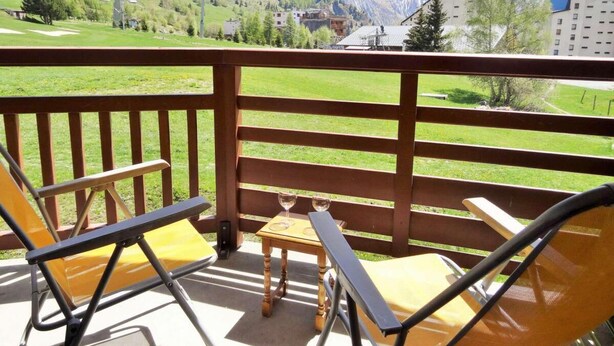 A balcony with wooden railings, two yellow chairs, a small table, and two wine glasses. - 100m from resort center, 2nd floor, view ski slopes, balcony, parking, tv, ski locker, 33m² (Les Deux Alpes)