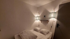 A small, cozy bedroom with a single bed, a nightstand, and two wall-mounted lamps. - 100m from resort center, 2nd floor, view ski slopes, balcony, parking, tv, ski locker, 33m² (Les Deux Alpes)