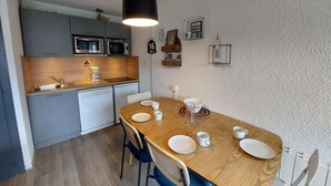 A compact kitchen with modern appliances, a dining area with a wooden table set for four, and a small island. - 100m from resort center, 2nd floor, view ski slopes, balcony, parking, tv, ski locker, 33m² (Les Deux Alpes)