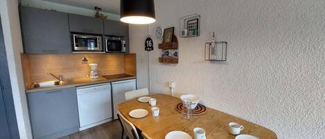 A compact kitchen with modern appliances, a dining area with a wooden table set for four, and a small island.