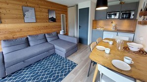 A modern living room with a grey sectional sofa, a wooden accent wall, and a dining area with a wooden table and chairs. - 100m from resort center, 2nd floor, view ski slopes, balcony, parking, tv, ski locker, 33m² (Les Deux Alpes)