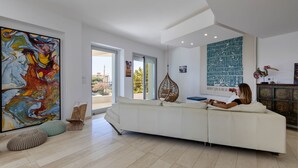 Un salon moderne avec un canapé blanc, un grand tableau abstrait et une vue sur l’extérieur.