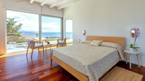 Une chambre avec un grand lit, une vue sur la mer et un balcon avec des meubles d’extérieur.