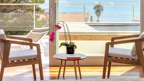 Un balcon avec deux chaises en bois, une petite table ronde et un pot de fleurs contenant une plante aux fleurs roses.