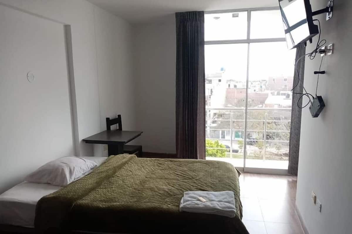 Een slaapkamer met een bed, een bureau en een raam met uitzicht op gebouwen.