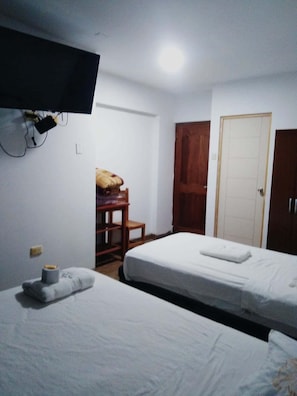 A room with two beds, a TV mounted on the wall, a wooden wardrobe, and a door. - Hotel Royal Olympic (Chiclayo)
