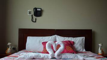 A hotel room with a bed, a telephone on the wall, and decorative items on the nightstand.