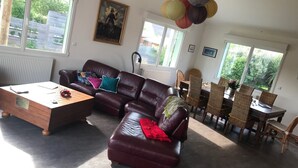 A living room with a brown leather sofa, a wooden coffee table, and a dining area with wicker chairs and a table.