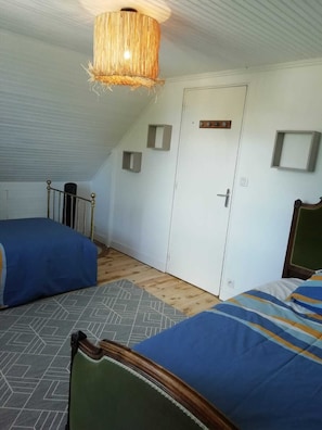 A room with two beds, a sloped ceiling, and a door with a small window.