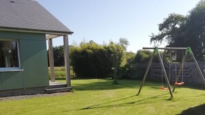 A grassy backyard with a swing set and a house with a covered porch.