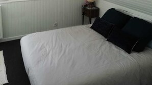 A bedroom with a sloped ceiling, a bed with white bedding, a nightstand with a lamp, and a framed picture on the wall.