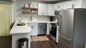 Une cuisine moderne avec des meubles blancs, des appareils en acier inoxydable et une table à manger en bois.