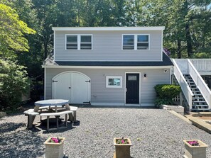 A two-story house with a front door, a small porch with a table and chairs, and a gravel driveway. - New 3Bd, 2BA Cottage short walk to Long Sands (York)