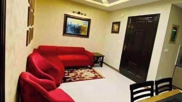 A living room with a red sofa, a dining table, and a kitchen area in the background. - 102 Luxury apartment to stay! (Lahore)