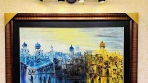 A framed painting of a cityscape with domed buildings and a bridge, mounted on a wall with a simple light fixture above it. - 102 Luxury apartment to stay! (Lahore)