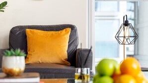 Un soggiorno moderno con un divano in pelle, un cuscino giallo, un tavolino in vetro con un libro, un bicchiere e una ciotola di frutta.