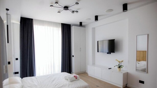 A modern hotel room with a large bed, a flat-screen TV mounted on the wall, and a minimalist design. - Sea On Mamaia (Constanța)