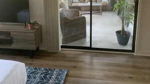 Ein Schlafzimmer mit Bett, Fernseher, einem Holzkapfen und einer großen Schiebetür, die auf eine Terrasse mit einer Couch, einem Sessel und einer Topfpflanze führt.
