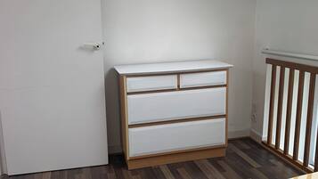 Un dormitorio con un aparador de madera, una cama con ropa de cama a rayas, un tragaluz y una puerta blanca.