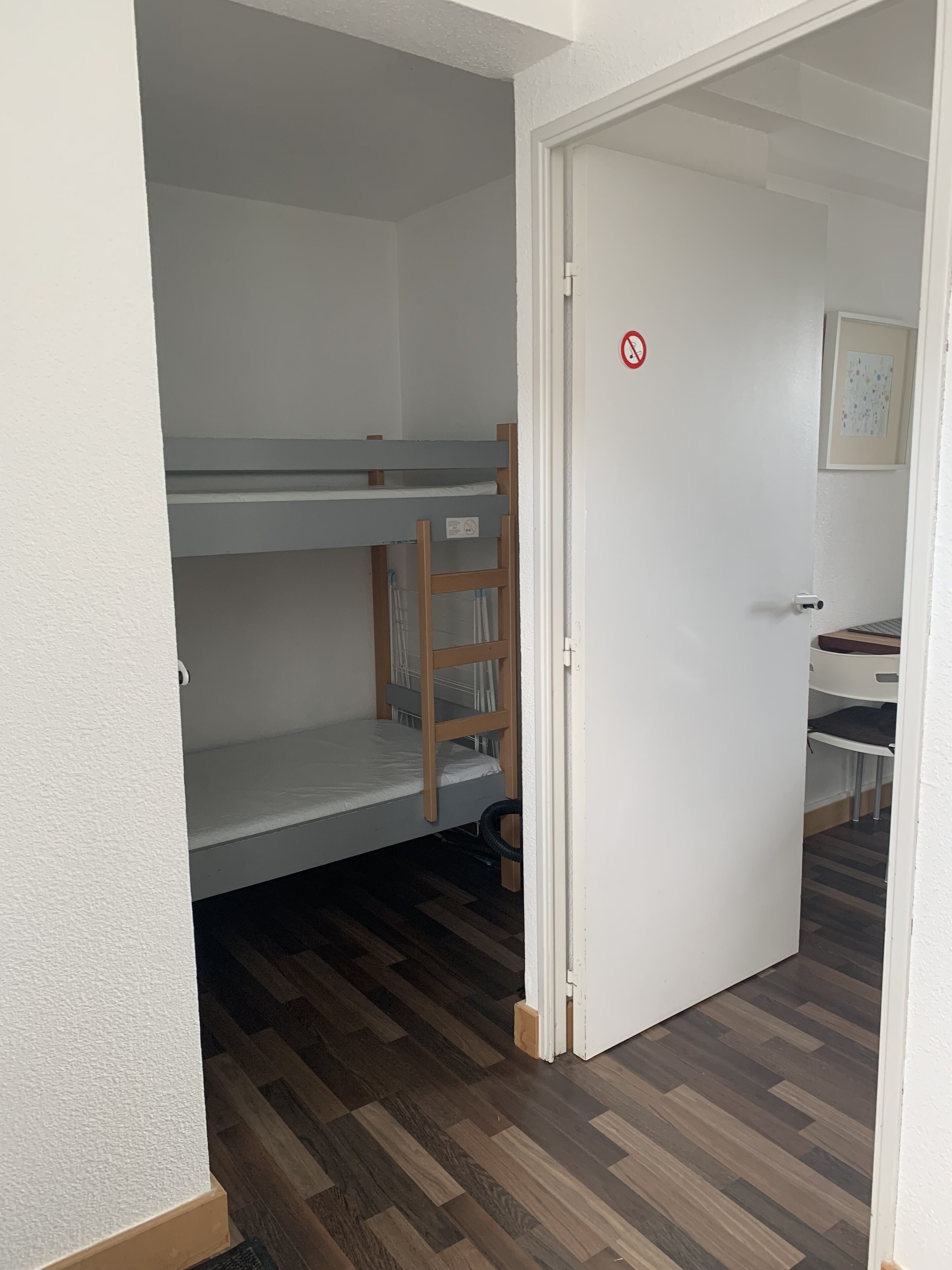 Una habitación con una cama individual superpuesta, una escalera de madera y una puerta con el letrero de prohibido fumar.