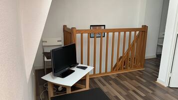 Ein Zimmer mit einem weißen Schreibtisch, einem schwarzen Monitor und einem Smartphone. Im Hintergrund ist ein Holzhandschiene und eine Treppe zu sehen.