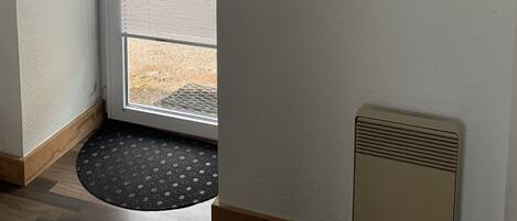 A room with a door leading to an outdoor area, a small rug at the entrance, and a wall-mounted air vent.