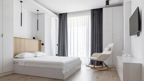 A modern hotel room with a large bed, a rocking chair, a small desk, and a TV. - Deluxe King Studio (Constanța)