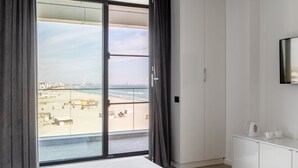 A bedroom with a large bed, a wardrobe, a television, and a view of the beach. - Deluxe King Studio (Constanța)