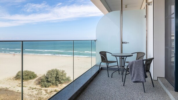 A balcony with a glass railing overlooking a beach. There are two chairs and a small table. - Deluxe King Studio (Constanța)