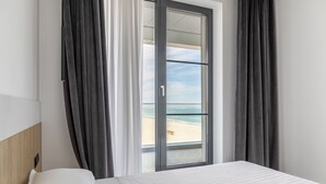 Une chambre d’hôtel avec un lit, une fenêtre donnant sur la plage et des rideaux gris.
