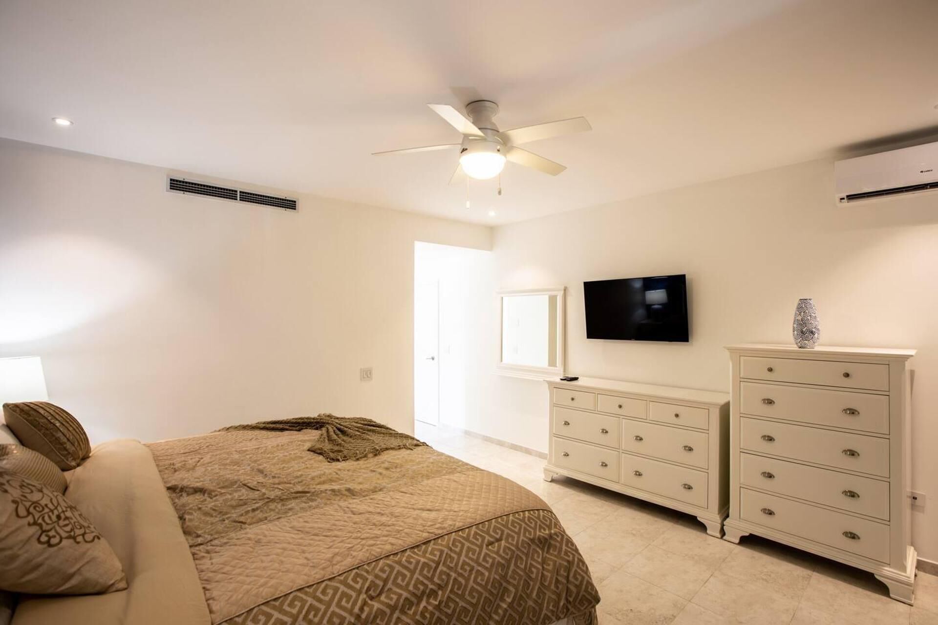 A bedroom with a bed, a ceiling fan, a TV, and a dresser.