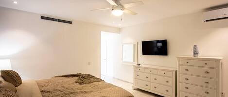 A bedroom with a bed, a ceiling fan, a TV, and a dresser.