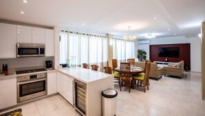 Eine moderne Küche mit Kochinsel, Essbereich mit Stühlen, einer Couch und einem Fernseher im Wohnzimmer.