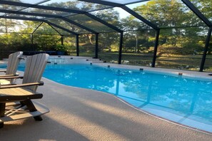 An indoor swimming pool with a glass enclosure, surrounded by lounge chairs and a view of trees. - 2 Bedroom Suite (Port Orange)