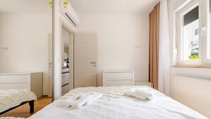 Ein Schlafzimmer mit einem Bett, einem Sessel, einem Kleiderschrank und einem Fenster mit Vorhängen.