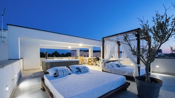 Ein modernes Schlafzimmer auf dem Dach mit einem großen Bett, einer kleinen Sitzecke und Blick auf die Stadt.