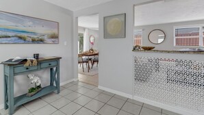 A modern interior with a teal console table, a painting of a beach, a decorative mirror, and a patterned screen. - Little Beach House w/ POOLandSPA - Vanderbilt Beach (Naples)