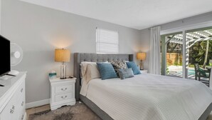 A bedroom with a large bed, two bedside tables, a TV, and a view of the outdoors. - Little Beach House w/ POOLandSPA - Vanderbilt Beach (Naples)