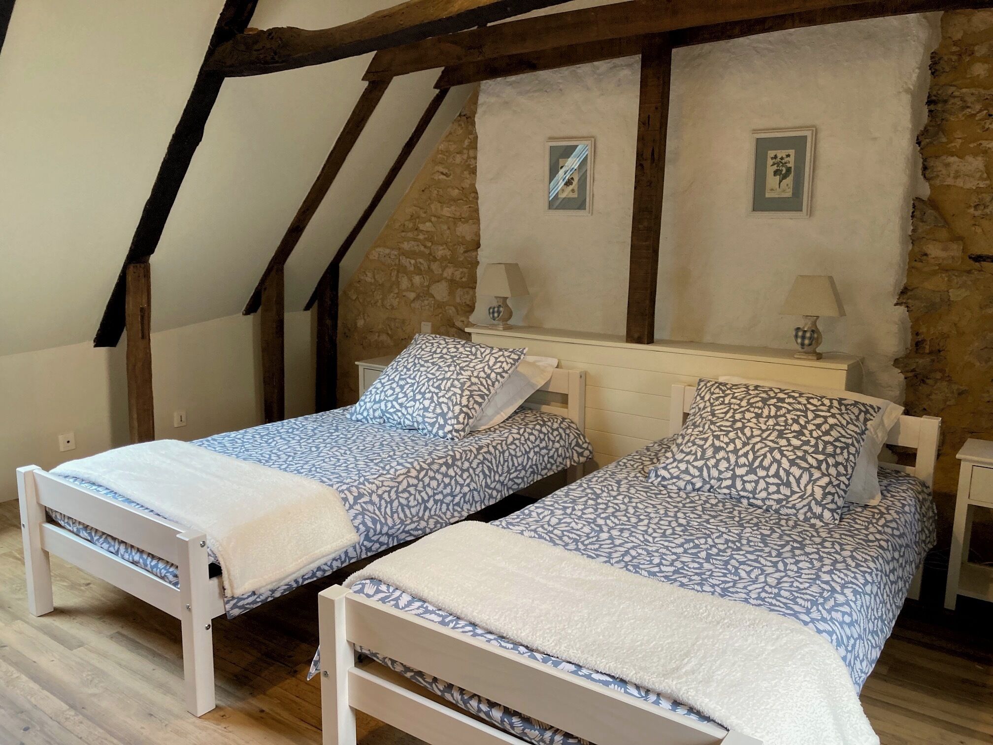 A bedroom with two single beds, wooden beams, stone walls, and two bedside lamps.
