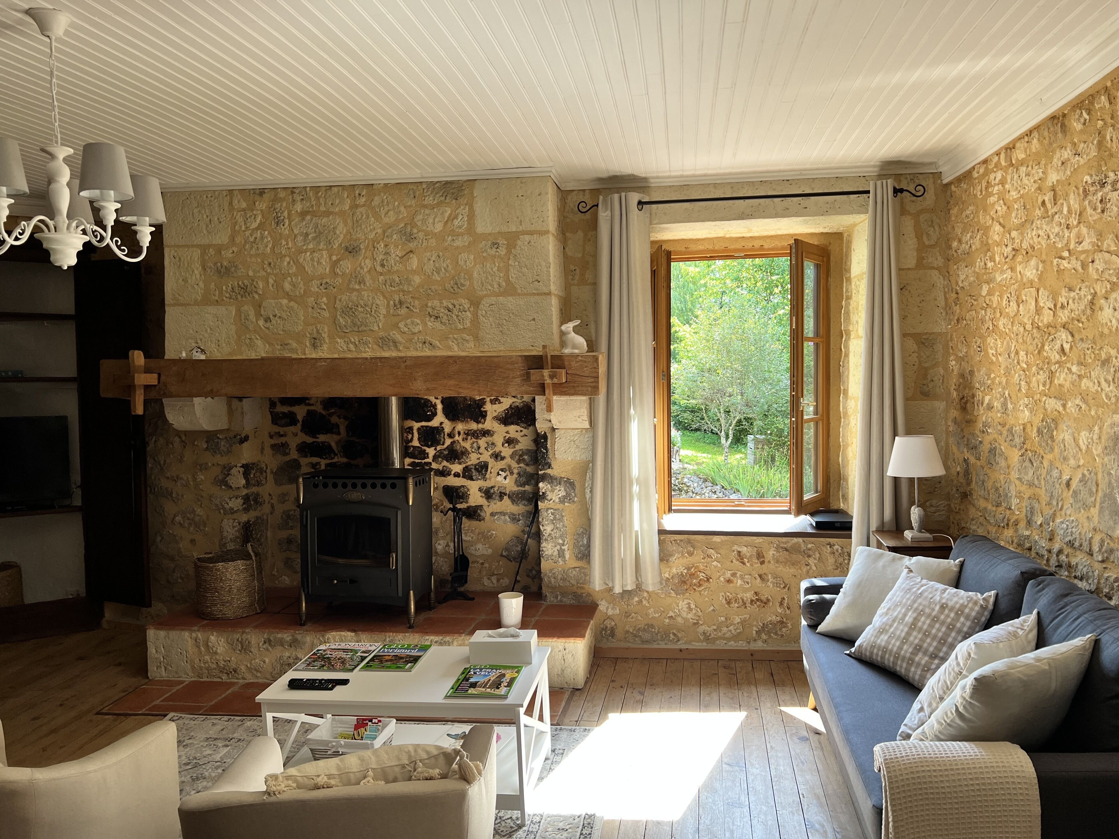 Ein gemütliches Wohnzimmer mit Steinwand, Kamin, einer Couch und einem Fenster mit Blick auf Grünflächen.