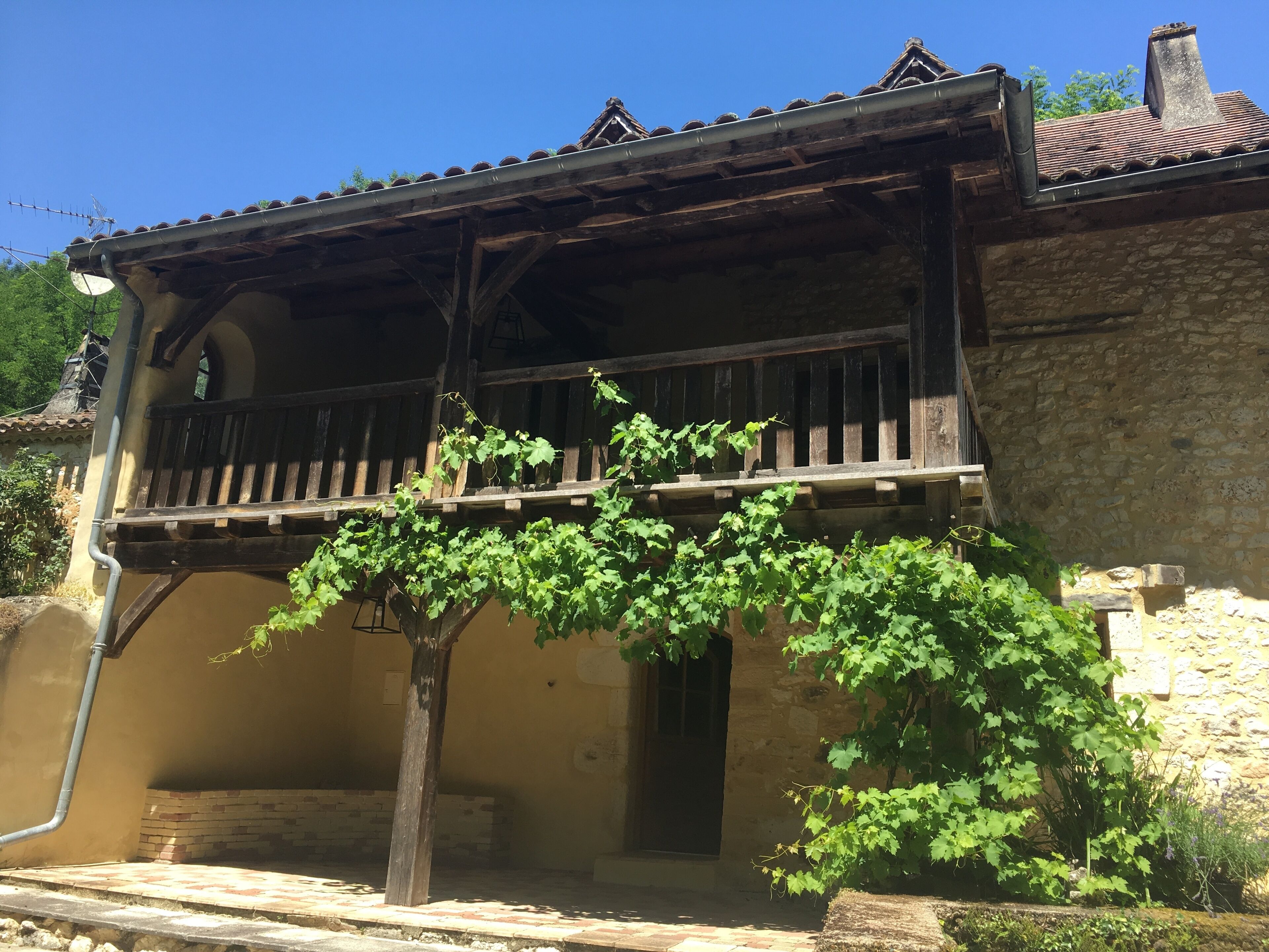 Un bâtiment rustique doté d’un balcon en bois, de murs en pierre et d’un arbre recouvert de lierre.