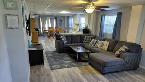 A living room with a sectional sofa, a coffee table, and a ceiling fan. There is a dining area with a table and chairs in the background. - We are the coolest hosts on the planet! You will love it here!  (Holiday)